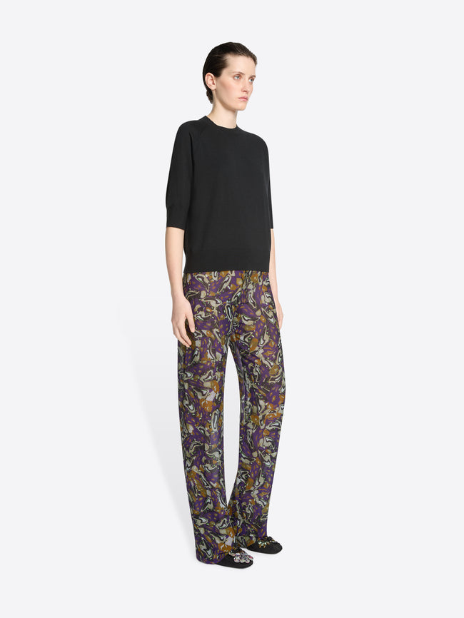 Person wearing a black top and patterned pants on a white background