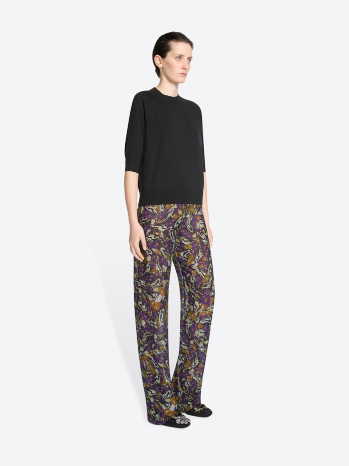 Person wearing a black top and patterned pants on a white background