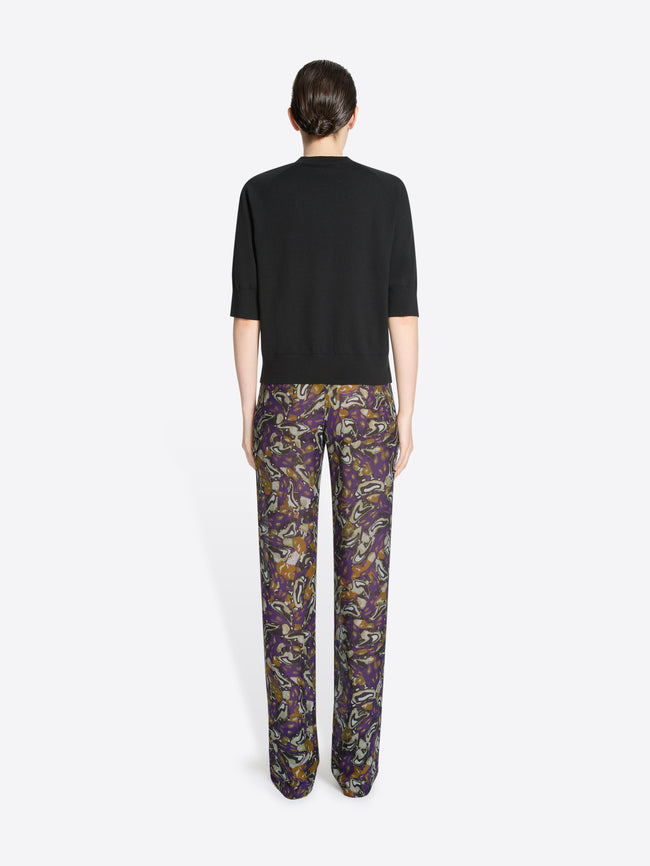 Back view of a person wearing a black top and patterned pants on a white background
