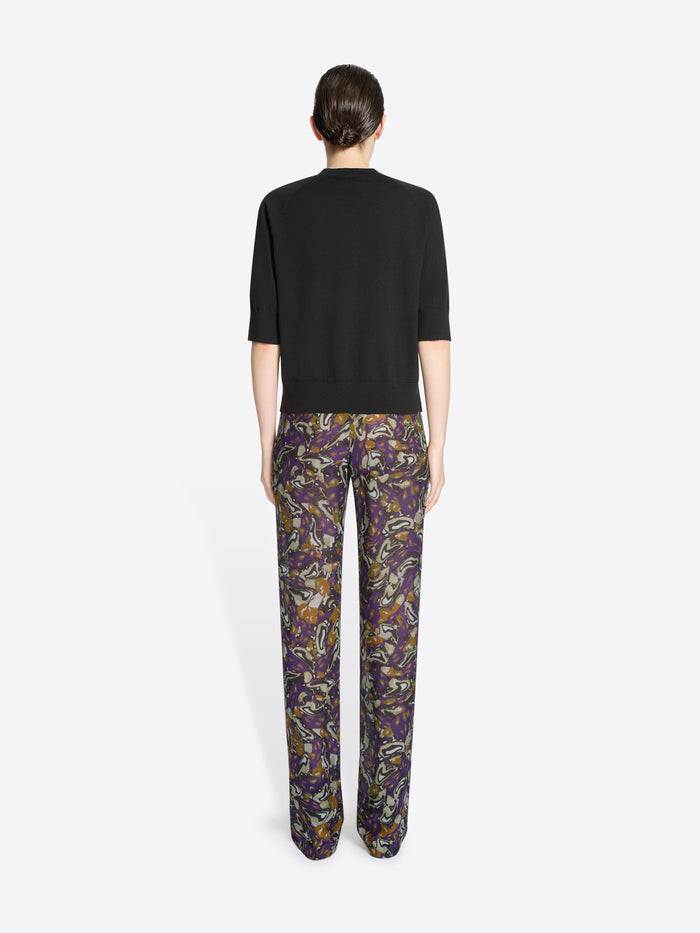 Back view of a person wearing a black top and patterned pants on a white background