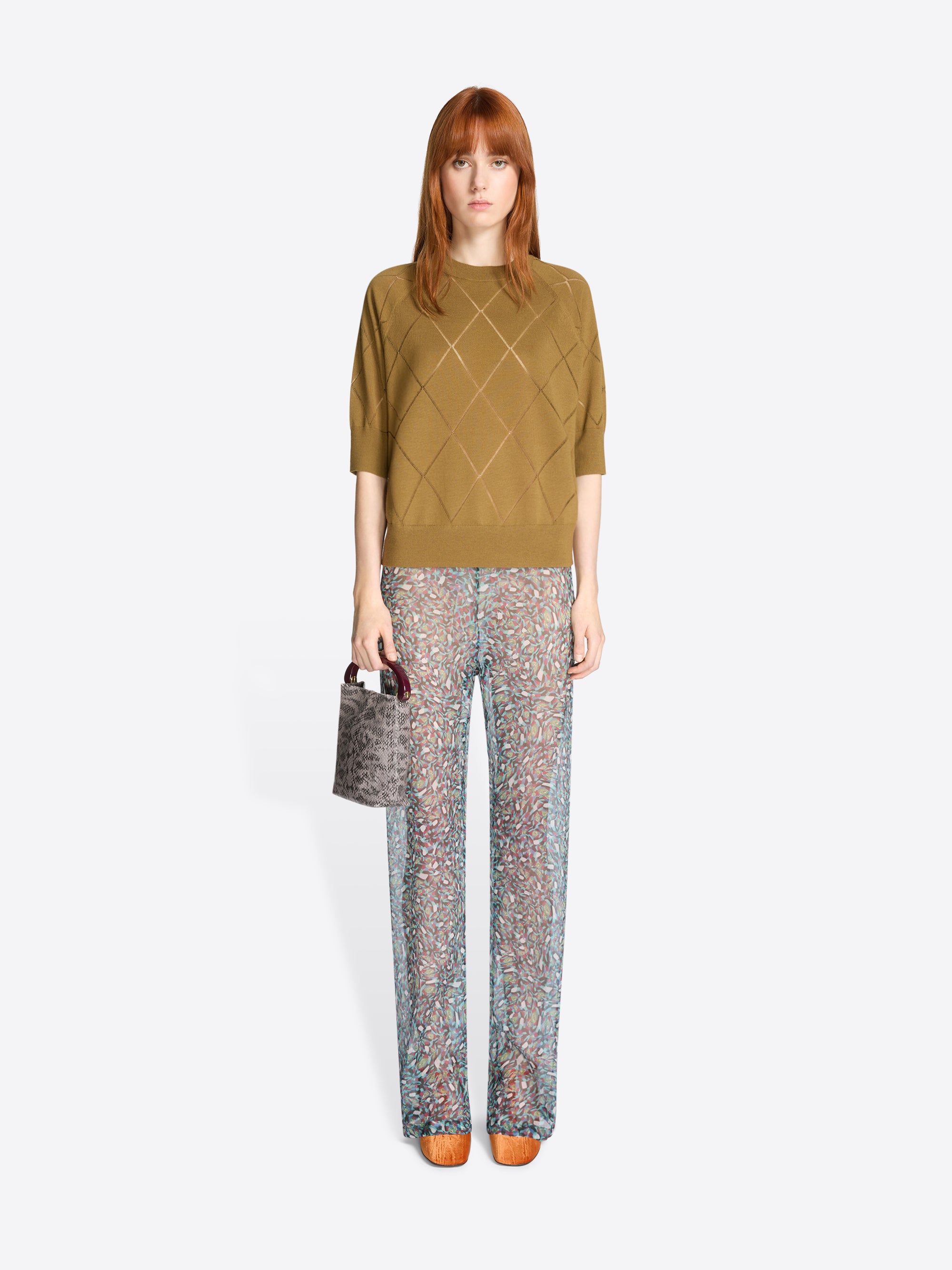 Woman wearing a mustard yellow knit top and patterned pants on a white background
