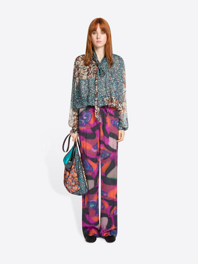 Woman wearing a patterned blouse and colorful pants with a handbag on a white background