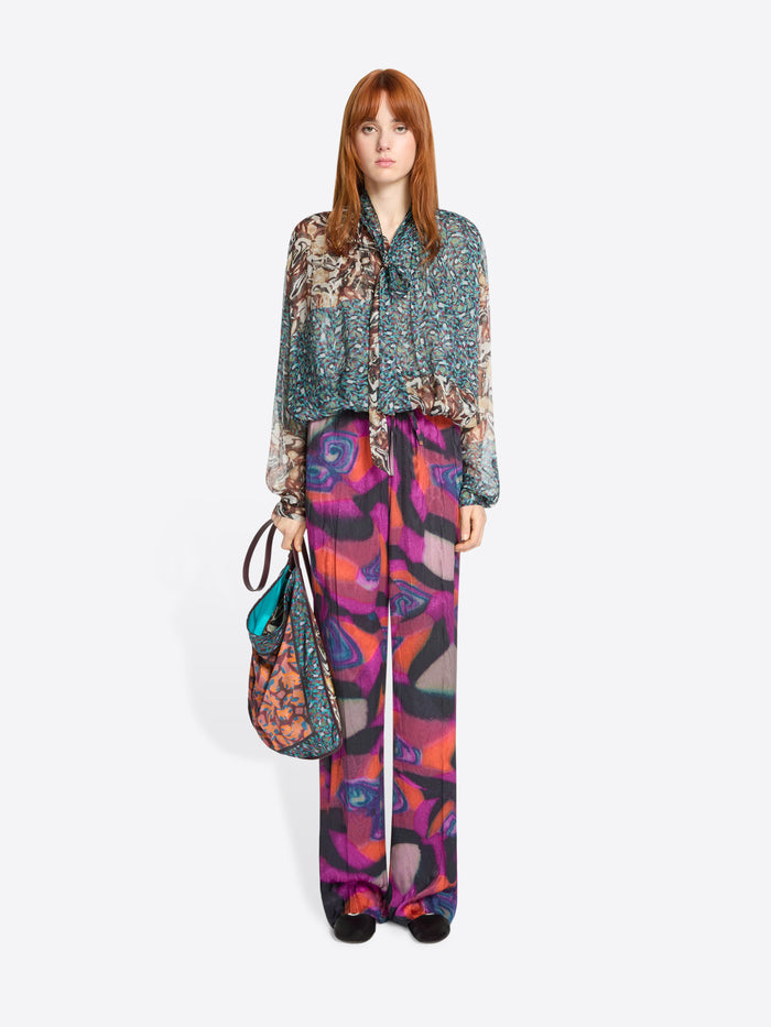 Woman wearing a patterned blouse and colorful pants with a handbag on a white background