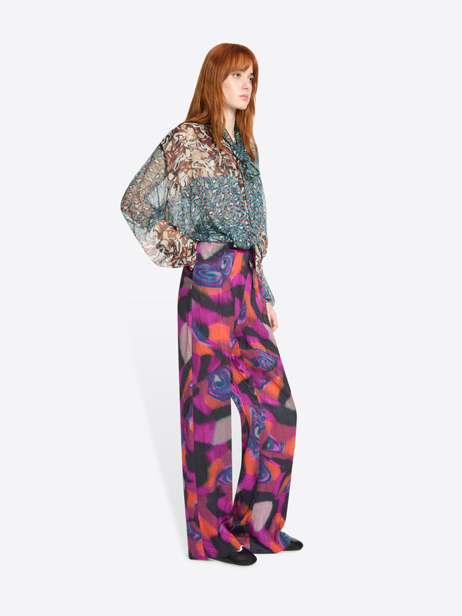 Woman wearing a patterned blouse and colorful pants on a white background