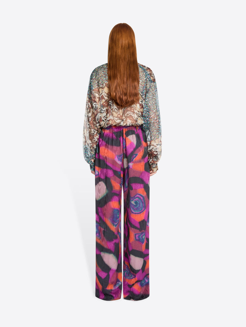Back view of a person wearing a patterned blouse and colorful pants on a white background