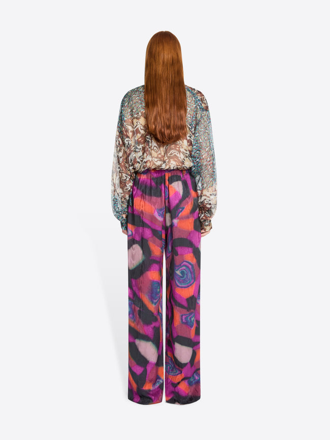 Back view of a person wearing a patterned blouse and colorful pants on a white background
