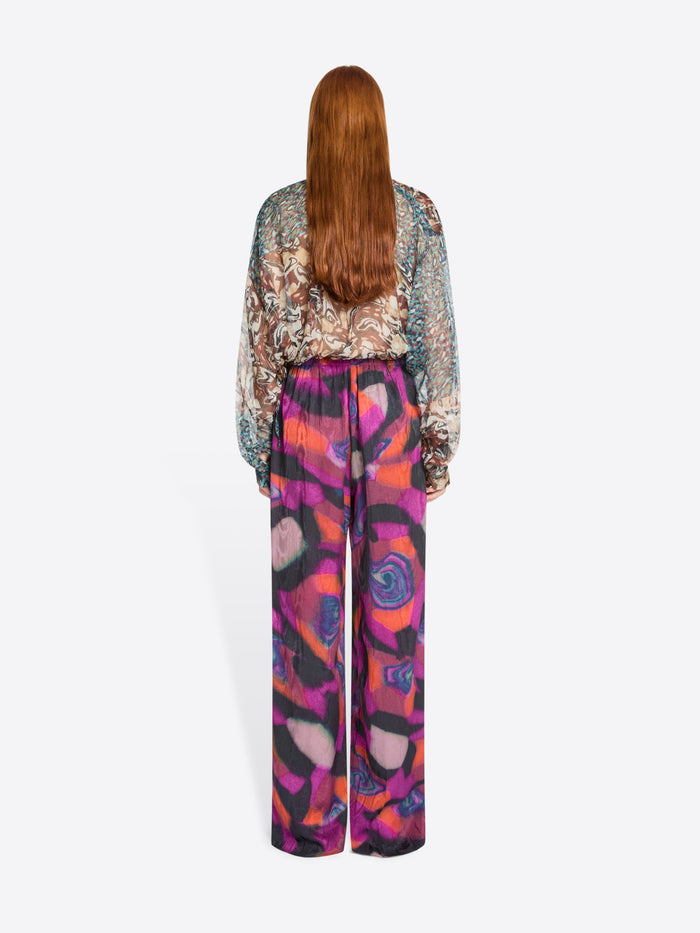 Back view of a person wearing a patterned blouse and colorful pants on a white background