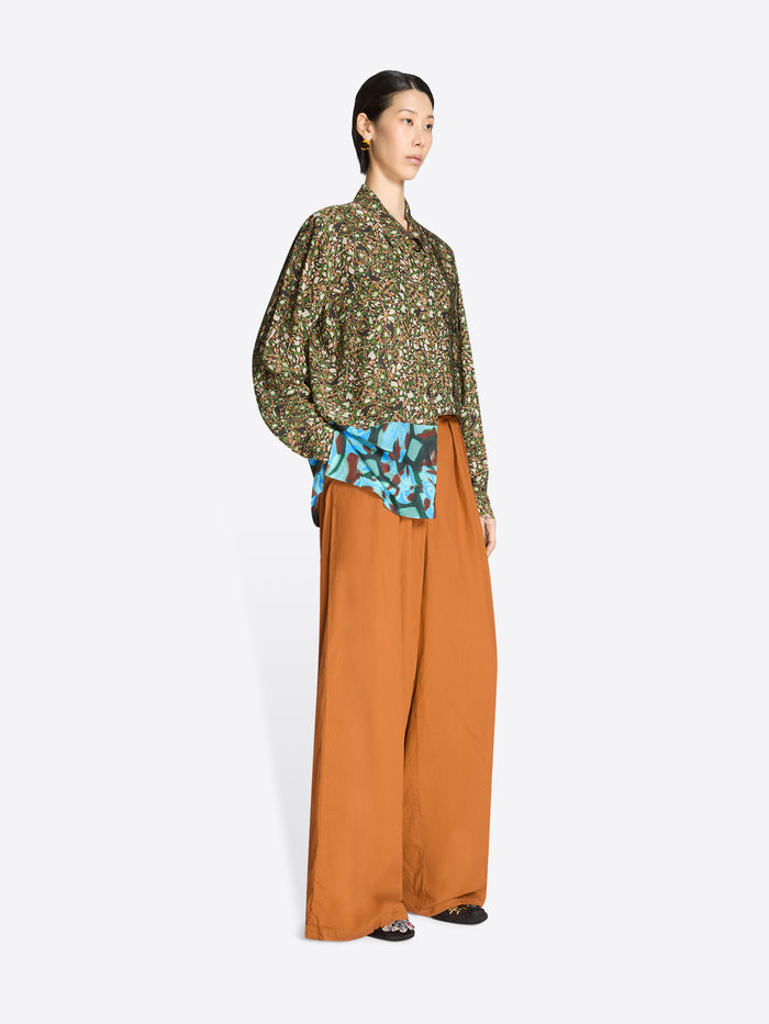 Woman wearing a patterned blouse and wide-leg orange pants on a white background