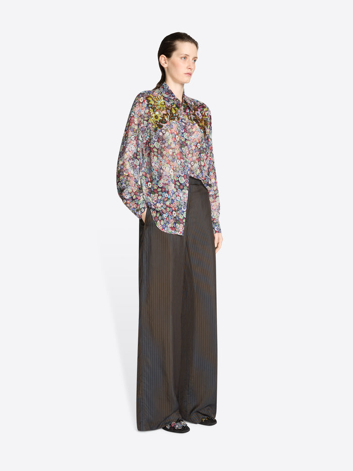 Model wearing a floral blouse and long dark pants on a white background