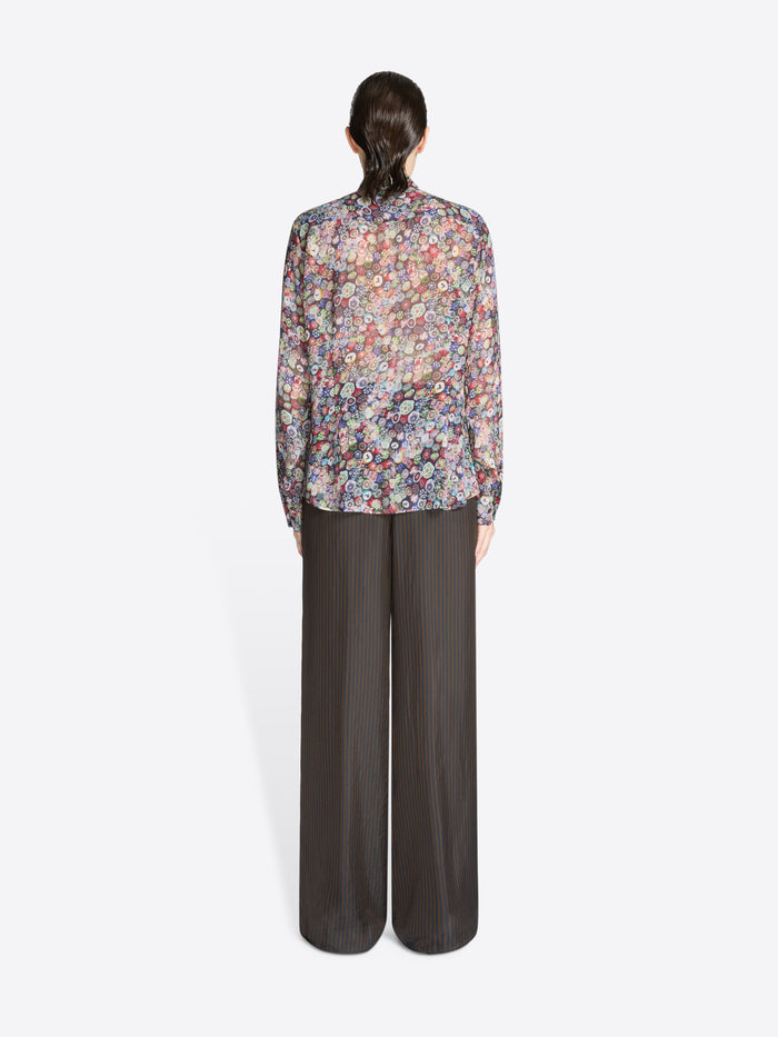 Back view of a person wearing a floral blouse and dark pants on a white background
