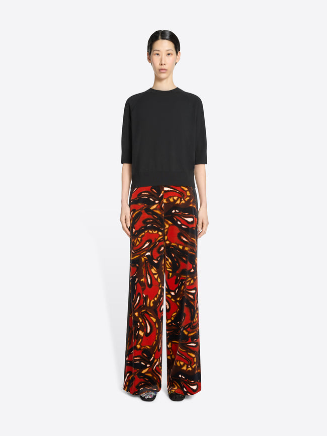 Person wearing a black top and colorful patterned pants on a white background