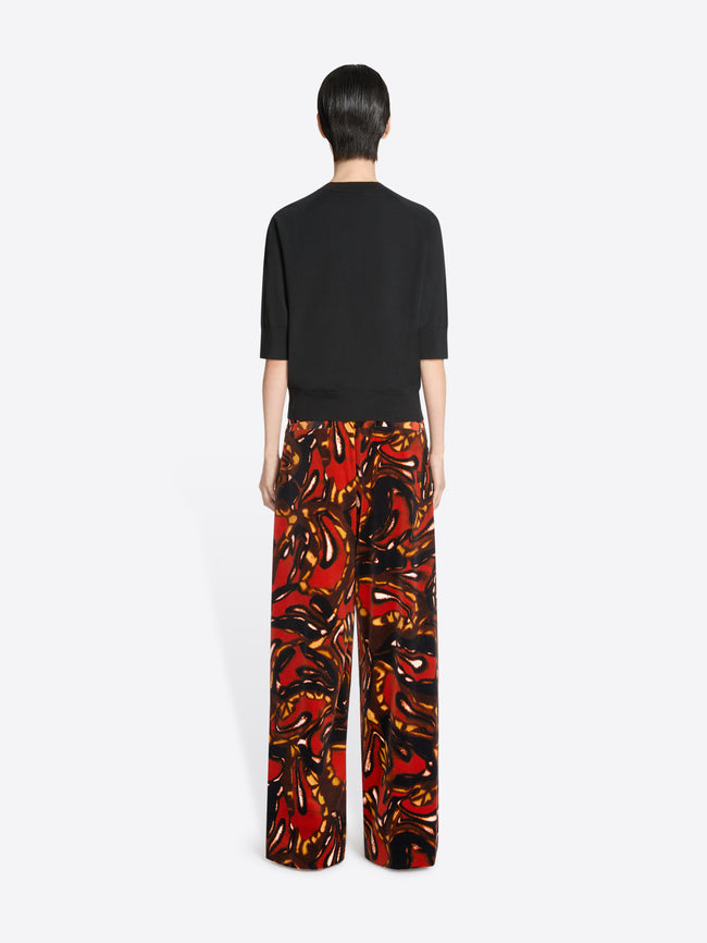 Back view of a person wearing a black top and colorful patterned pants on a white background