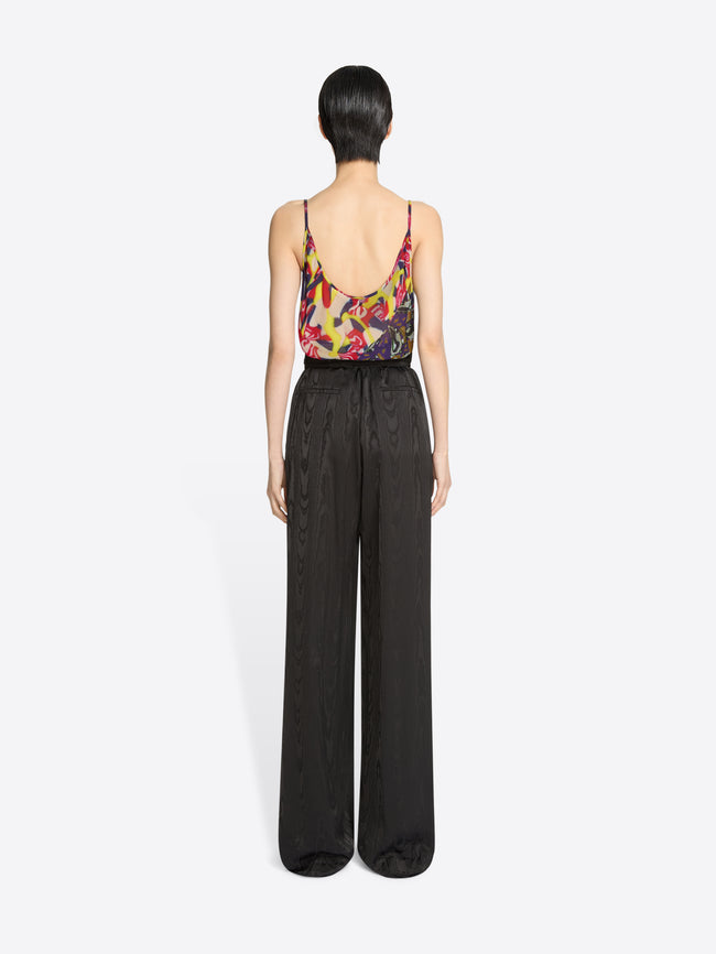 Back view of a person wearing a colorful top and dark brown pants on a white background