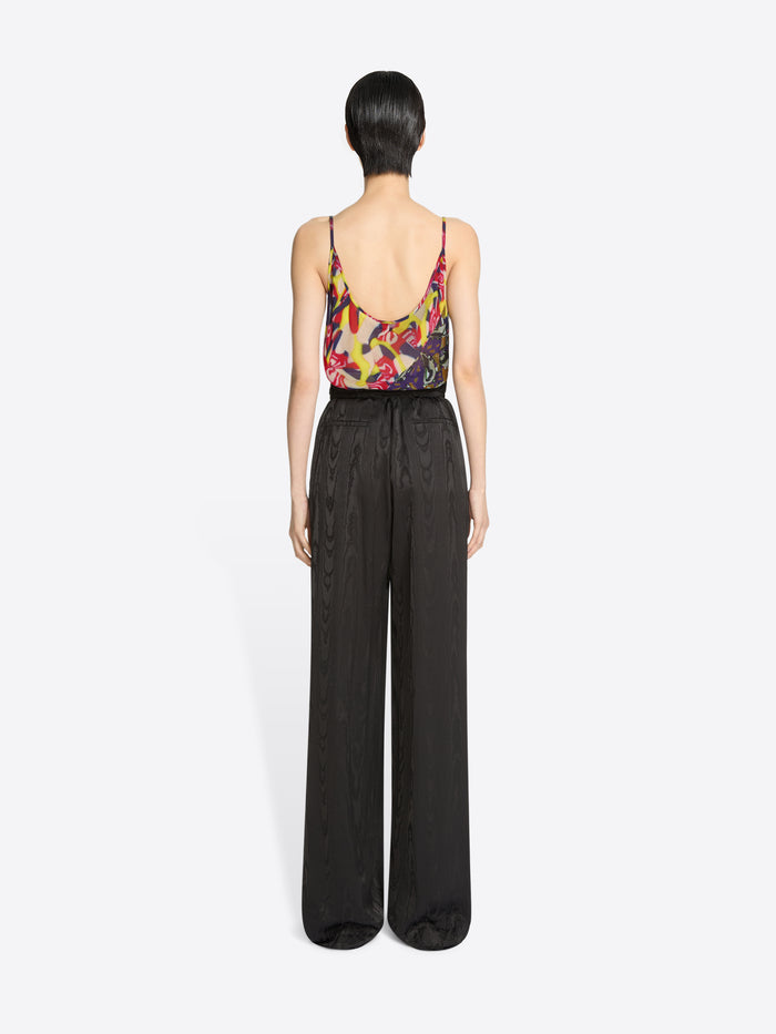 Back view of a person wearing a colorful top and dark brown pants on a white background