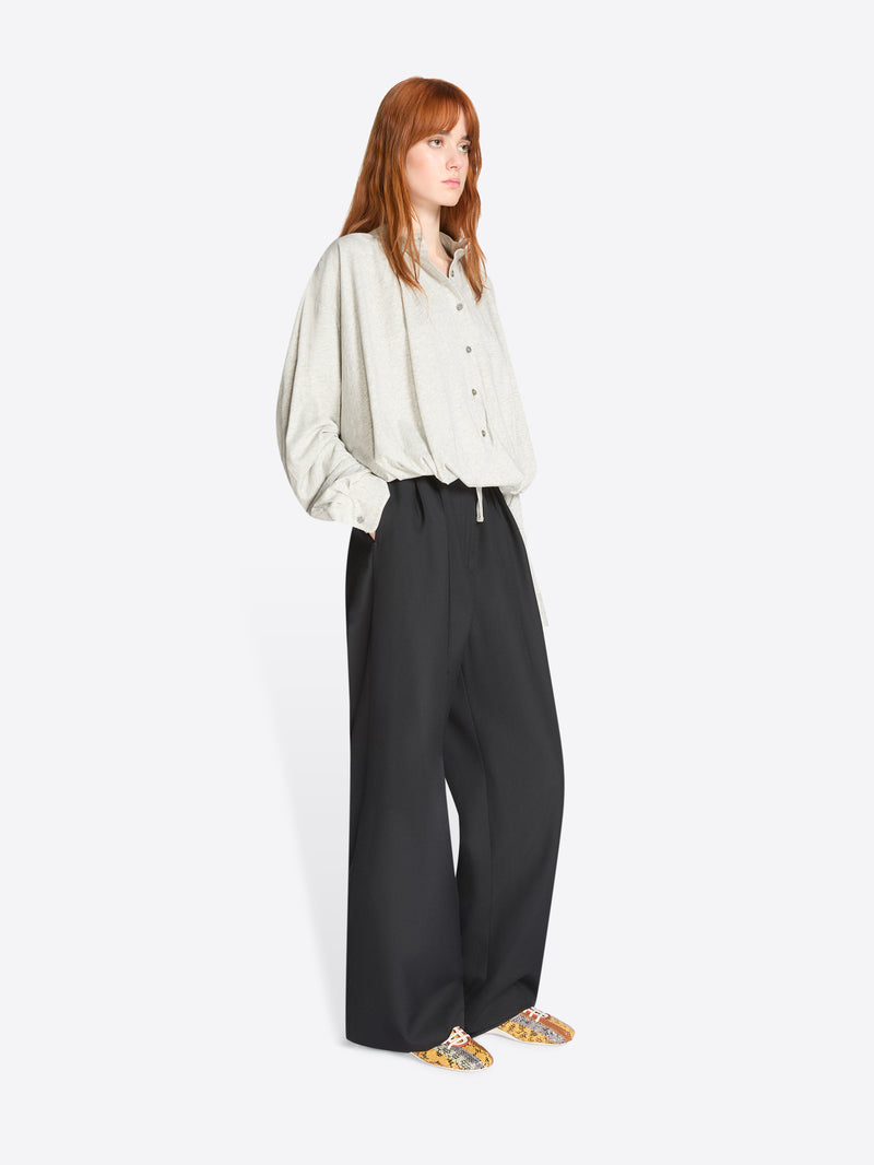 Person wearing a light-gray shirt and black pants on a white background