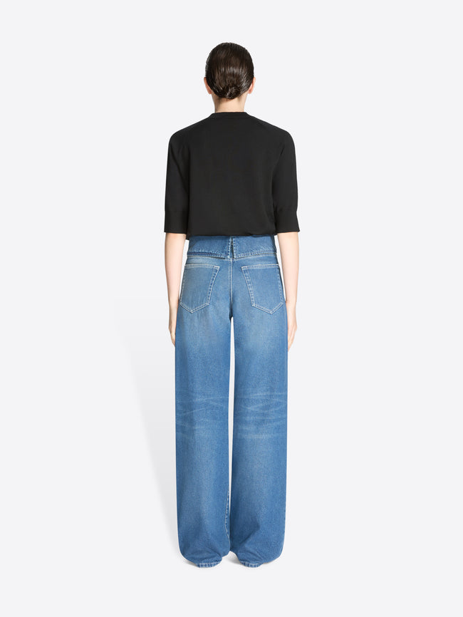 Back view of a person wearing blue jeans and a black top on a white background