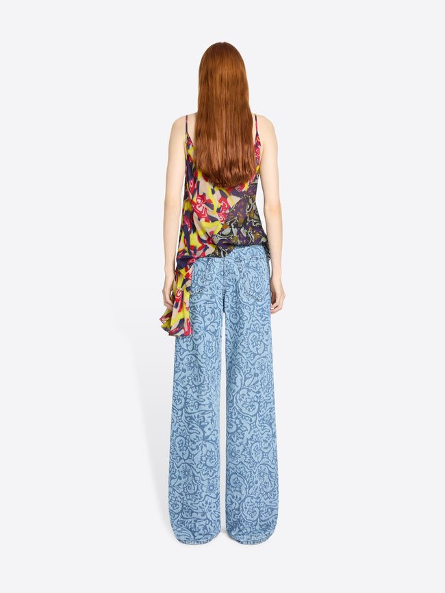 Back view of a woman wearing a colorful sleeveless top and blue patterned pants on a white background
