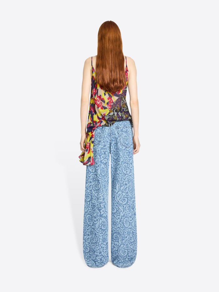 Back view of a woman wearing a colorful sleeveless top and blue patterned pants on a white background