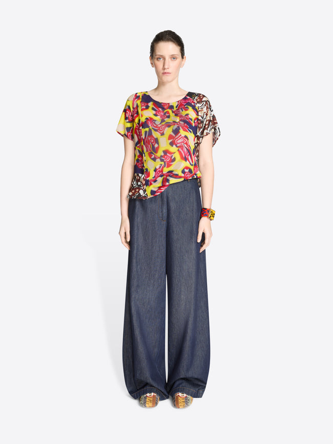 Woman wearing a colorful floral top and dark blue wide-leg denim pants on a white background