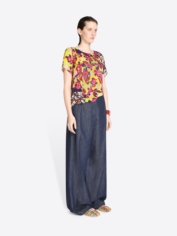 Woman wearing a colorful floral top and dark blue denim pants on a white background