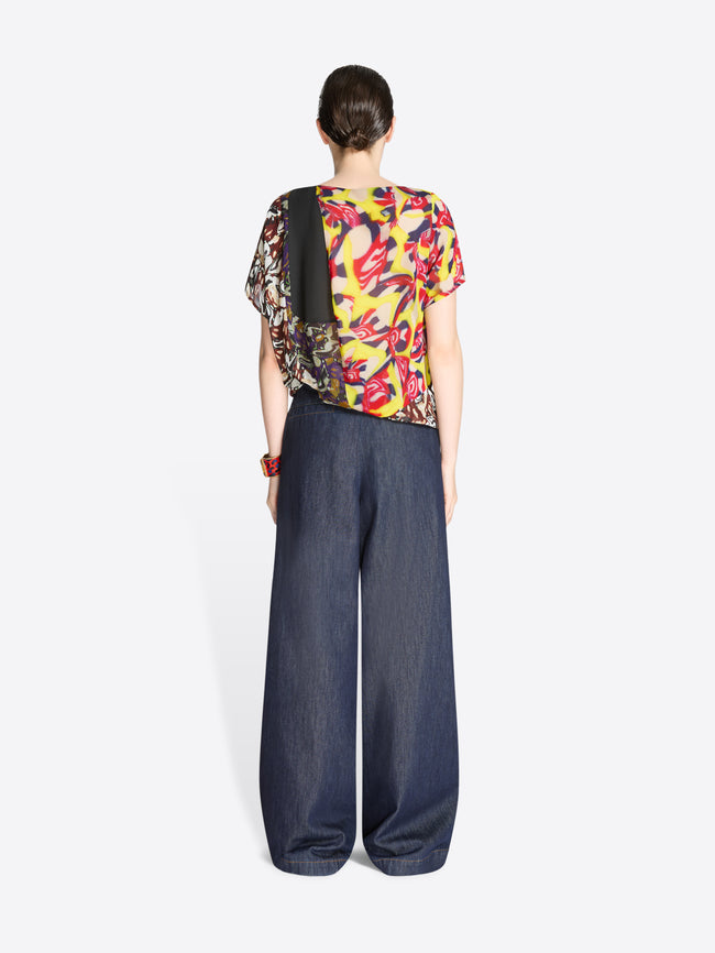 Back view of a person wearing a colorful top and dark blue denim pants on a white background