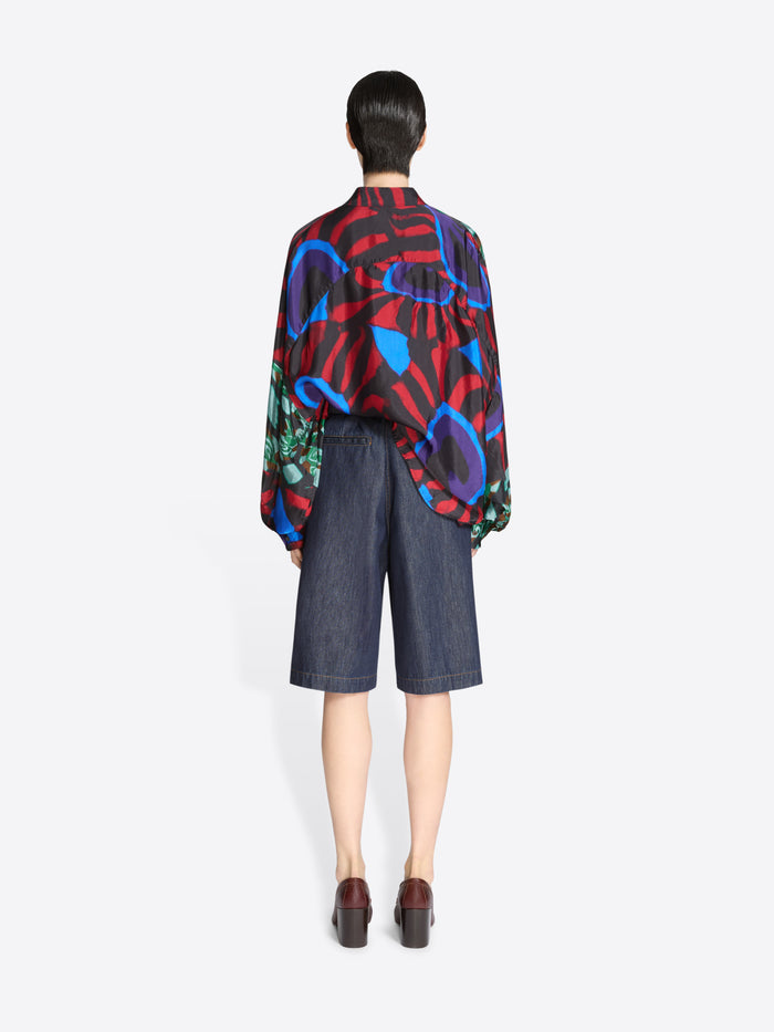 Back view of a person wearing a colorful abstract patterned shirt and dark denim shorts on a white background