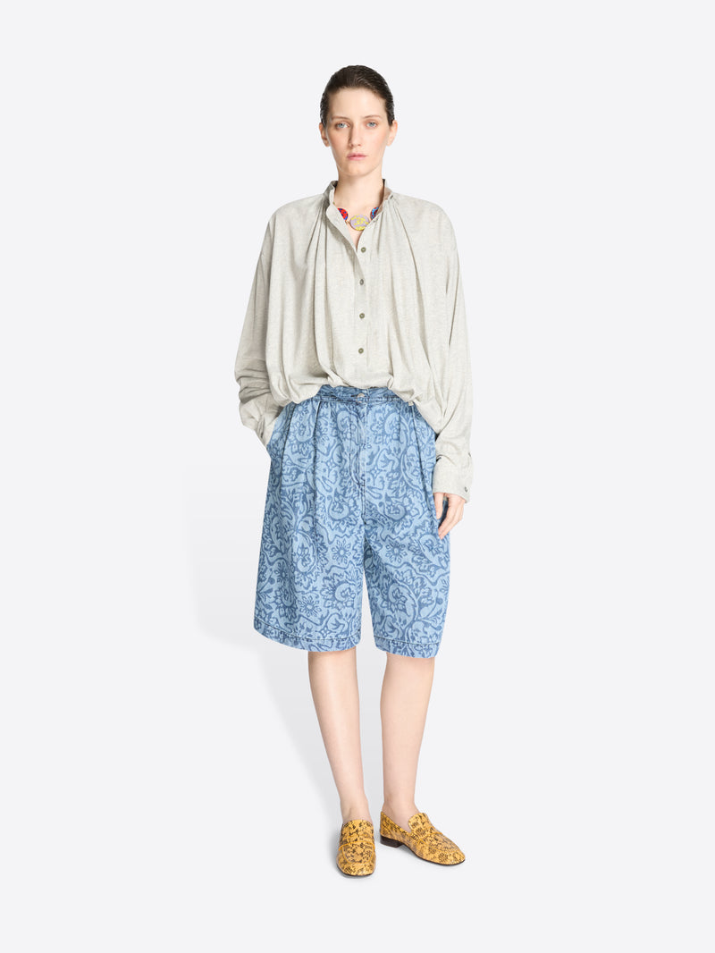 Woman wearing a light-colored shirt and blue patterned shorts on a white background