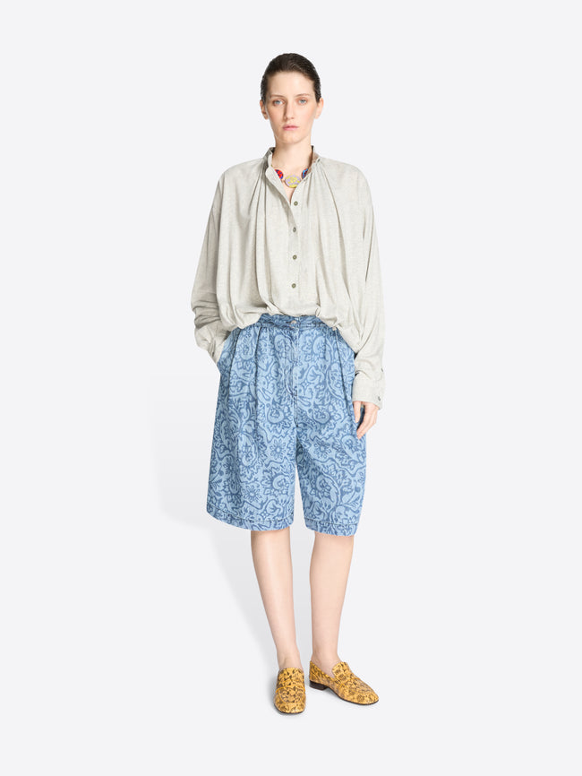 Woman wearing a light-colored shirt and blue patterned shorts on a white background