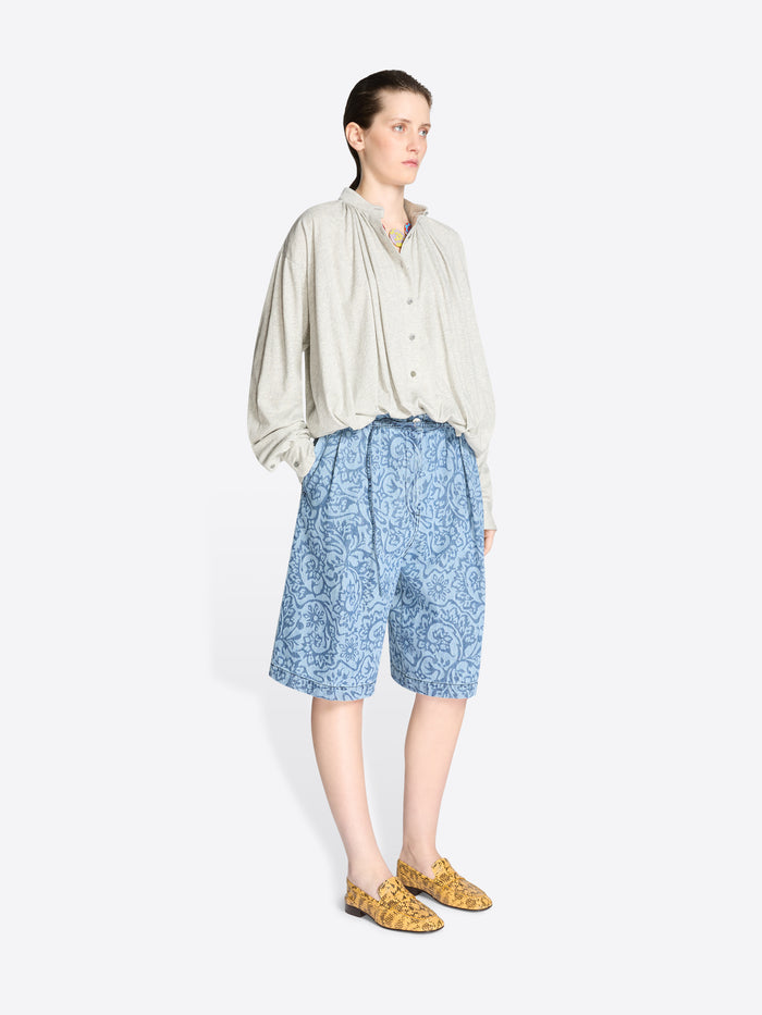 Person wearing a light-colored shirt and blue patterned shorts on a white background