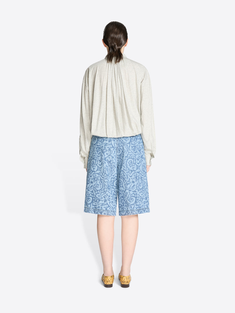 Back view of a person wearing a light-colored shirt and blue patterned shorts on a white background