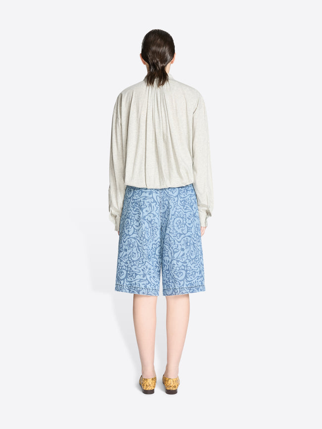 Back view of a person wearing a light-colored shirt and blue patterned shorts on a white background