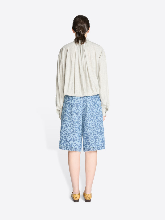 Back view of a person wearing a light-colored shirt and blue patterned shorts on a white background
