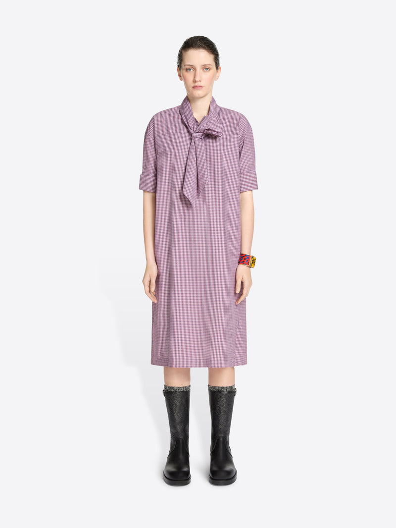 Woman wearing a purple checkered dress with a tie-neckline on a white background