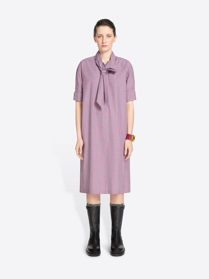 Woman wearing a purple checkered dress with a tie-neckline on a white background