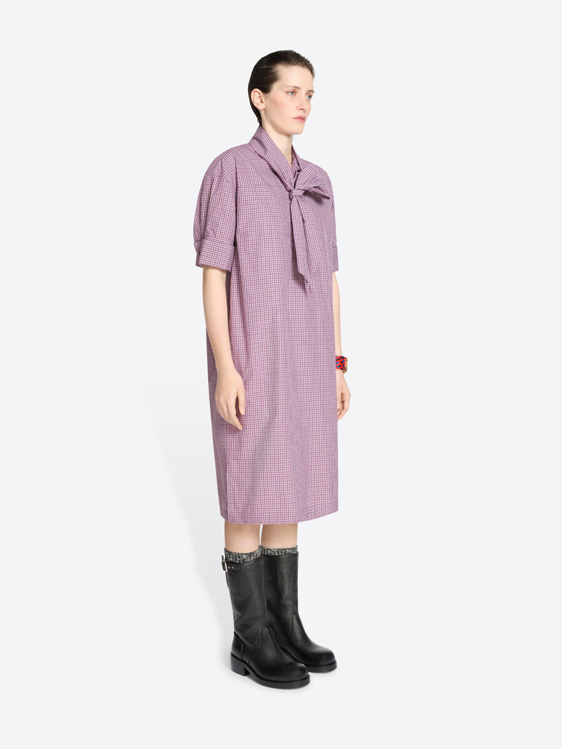 Woman wearing a purple checkered dress with a tie detail on a white background