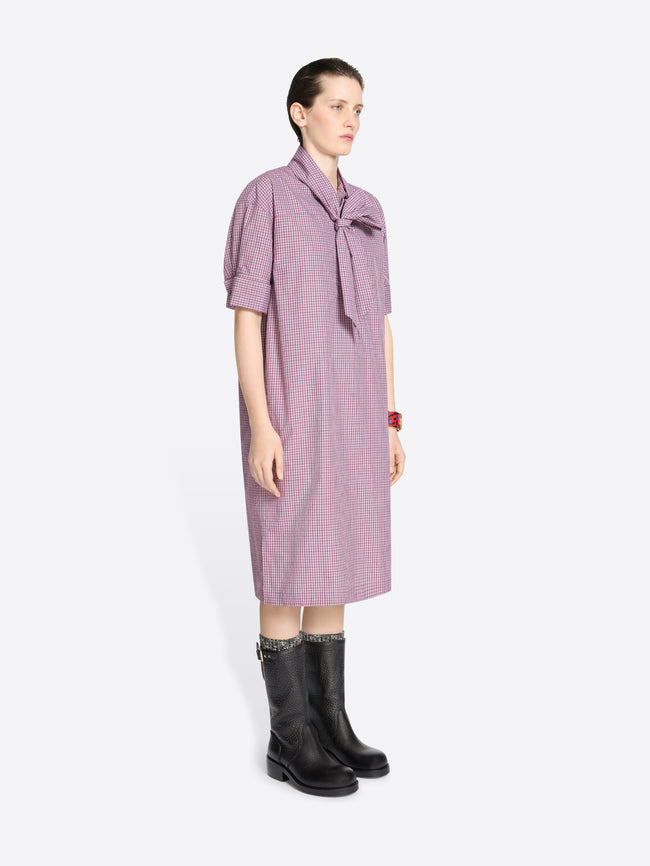 Woman wearing a purple checkered dress with a tie detail on a white background