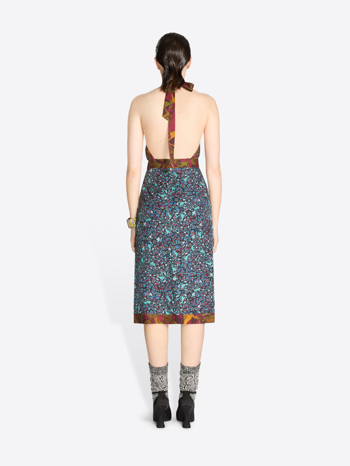 Back view of a woman wearing a patterned dress with open back on a white background