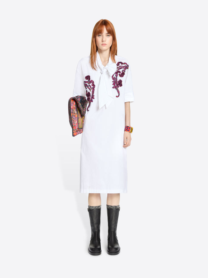 Woman wearing a white dress with purple floral embroidery and black boots on a white background