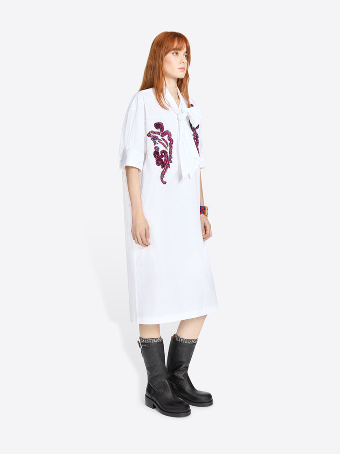 Woman wearing a white dress with purple floral embroidery on a white background
