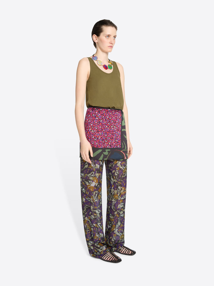 Woman wearing a green sleeveless top, skirt and patterned pants on a white background
