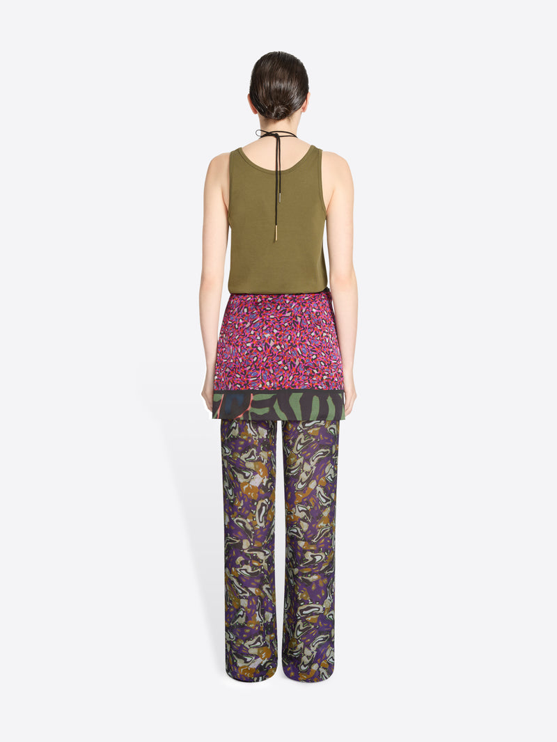 Back view of a person wearing a green top, skirt and patterned pants on a white background