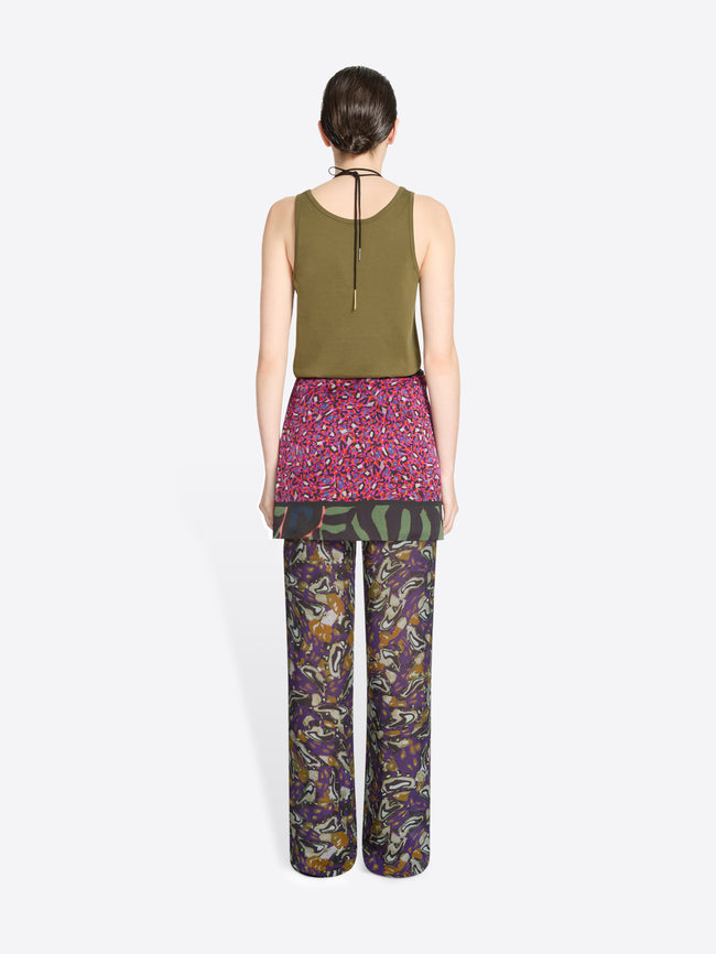 Back view of a person wearing a green top, skirt and patterned pants on a white background