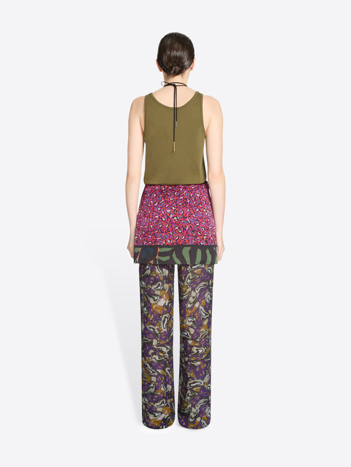 Back view of a person wearing a green top, skirt and patterned pants on a white background