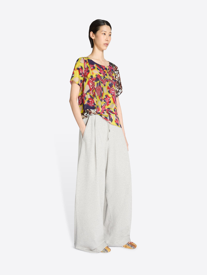 Woman wearing a colorful floral blouse and light-colored pants on a white background