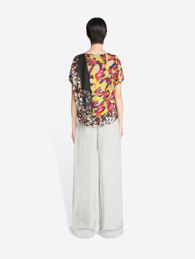 Back view of a person wearing a colorful floral top and white pants on a white background