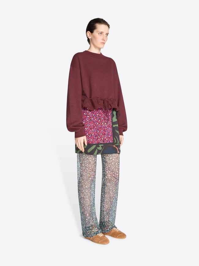 Person wearing a burgundy sweatshirt, skirt and patterned pants on a white background