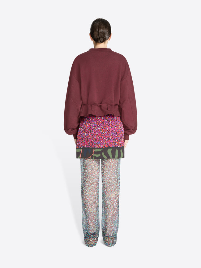 Back view of a person wearing a burgundy sweatshirt and patterned pants on a white background