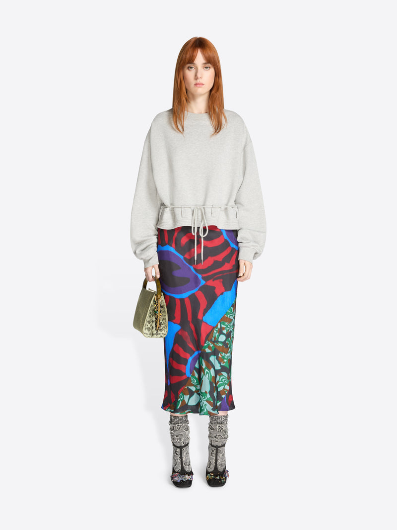 Woman wearing a light gray sweatshirt and colorful patterned skirt on a white background