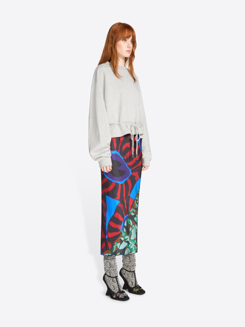 Woman wearing a colorful skirt with abstract patterns and light gray sweatshirt on a white background