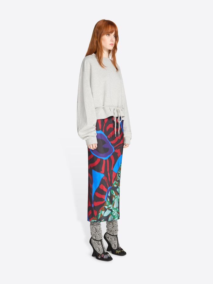 Woman wearing a colorful skirt with abstract patterns and light gray sweatshirt on a white background